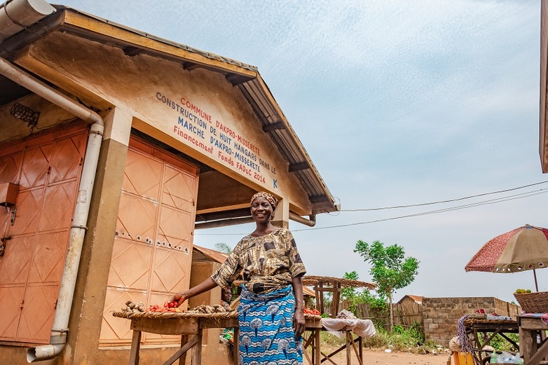 Une femme, souriante, se tient devant son étal de marché dont la construction a été financée par des investissements.