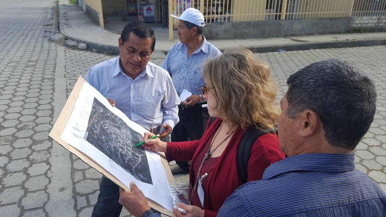 Four people stand on the street looking at a satellite image of the city.