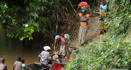  People loading a boat at the edge of a forest.