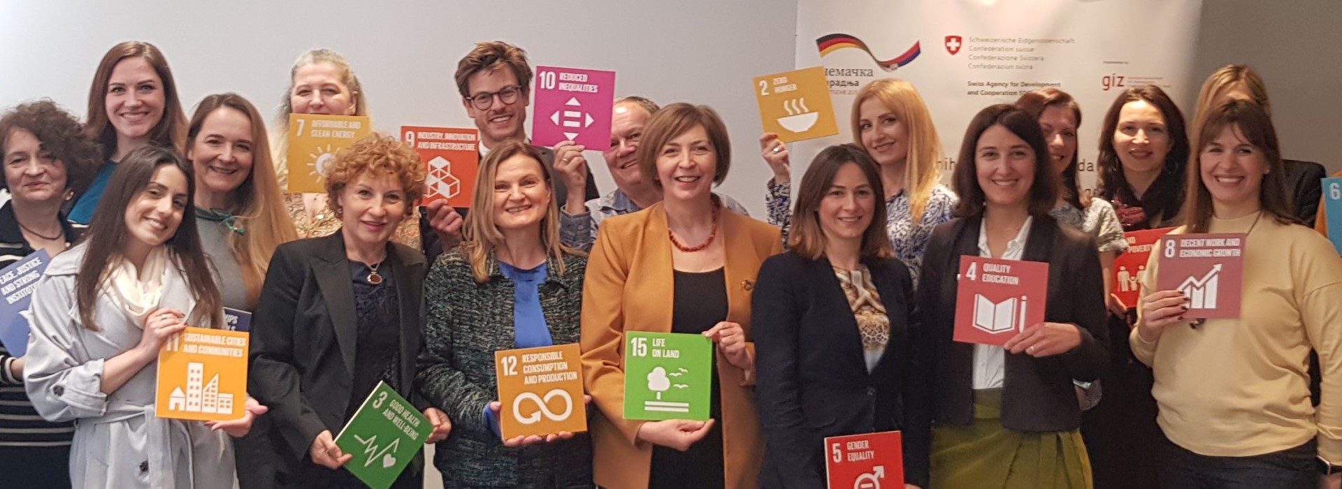 Women stand together holding signs with the Sustainable Development Goals.