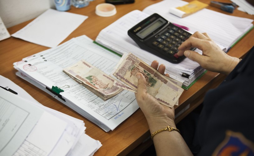 A person holds money in her hand and types on a calculator.