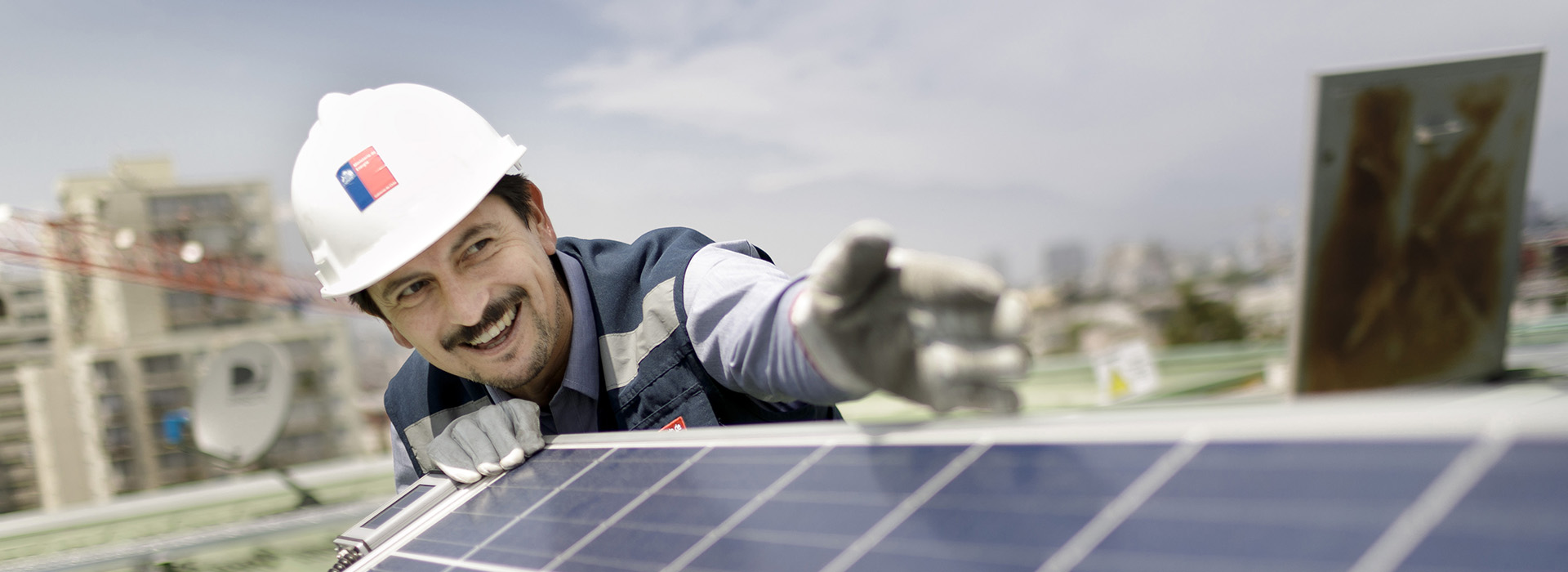 A construction worker wearing a hard hat works on a solar panel.