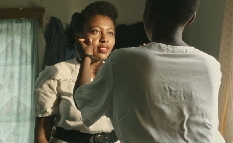 A woman in a white dress looks into the eyes of another woman who is touching her cheek.